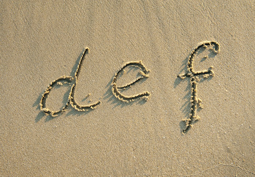 alphabet letters handwritten in sand on beach