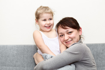 Mother and her little daughter sitting and couch and hugging