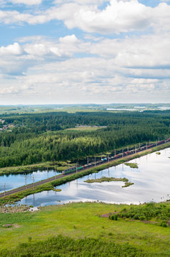 Freight train passes at double line railroad with electric poles in evergreen wood and lakes. Aerial view. Northern Oktyabrskaya Railway