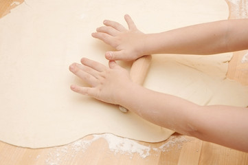 Child's hands kneading dough on wooden table