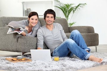 Couple sat on couch with laptop and newspaper