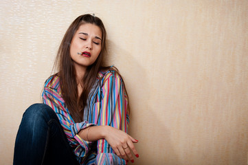 Fototapeta premium Depressed woman sitting by the wall with cigarette in mouth