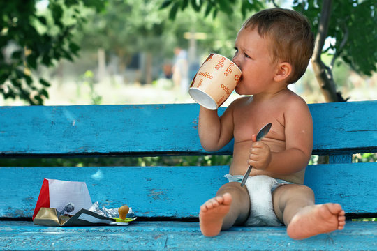 Baby Boy Sitting On Rural Bench Drinking Coffee With Chocolate