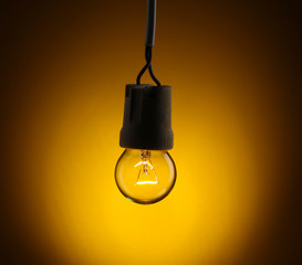 A lit light bulb on yellow background