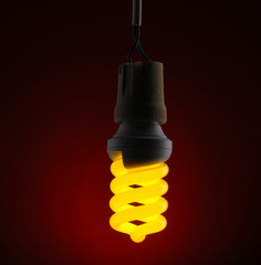 A lit energy saving light bulb on red background