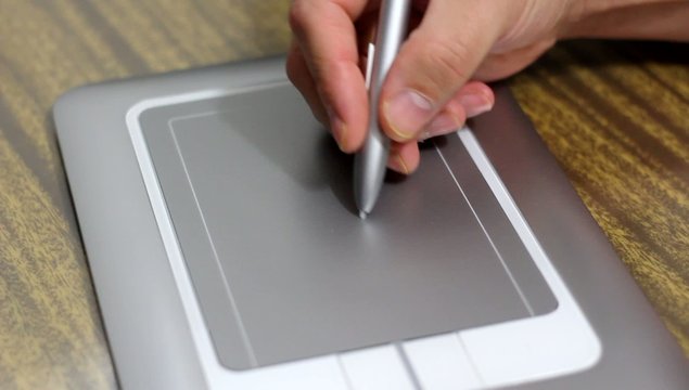 Man draws a pen on tablet lying on table close up
