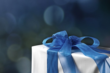Gift box with blue ribbon, soft defocused lights background