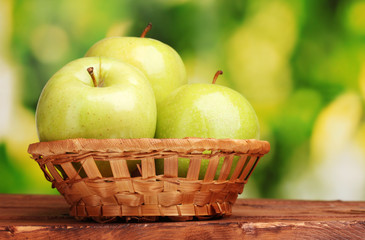 juicy green apples in basket on wooden table on green background