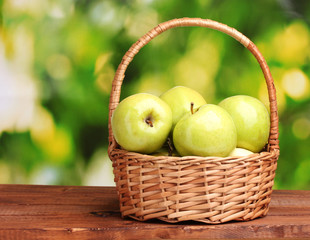 juicy green apples in basket on wooden table on green background