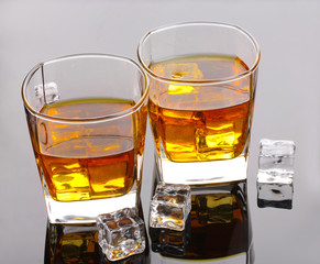 two glasses of scotch whiskey and ice on grey table