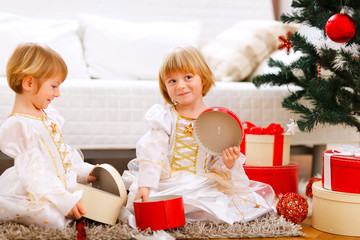 Obraz na płótnie Canvas Two smiling twins girl opening presents near Christmas tree