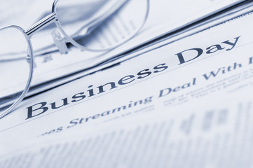 Eyeglasses lie on the newspaper with title Business day. Blue to