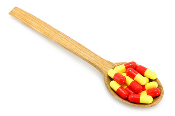 Wooden spoon with pills on a white background