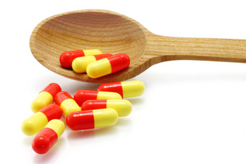 Wooden spoon with pills on a white background