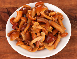 Marinated mushrooms in saucer on wooden table