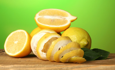 ripe lemons with leaves on wooden table on green background