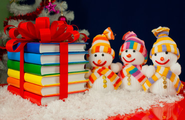 Stack of colorful books tied up with red ribbon and three snowme
