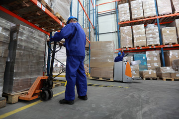 Two workers in uniforms and safety helmets working in storehouse