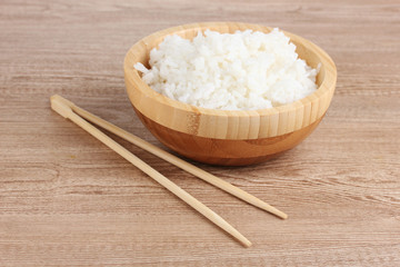 Wooden bowl of cooked rice and chopsticks on wooden table