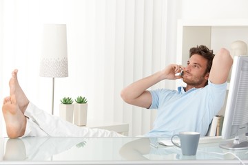 Relaxed man talking on mobile phone at desk