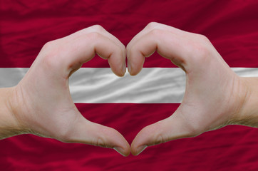 Heart and love gesture showed by hands over flag of latvia backg