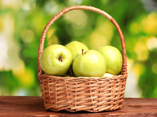 juicy green apples in basket on wooden table on green background