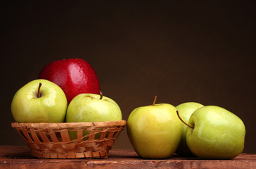 juicy sweet apples in basket on wooden table on brown background