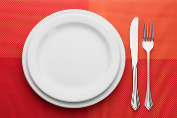White empty plate with fork and knife on a red tablecloth