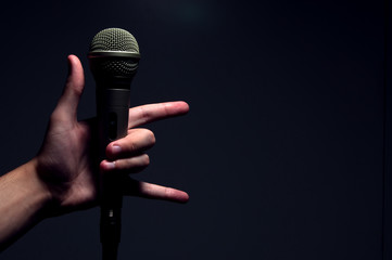 Mão segurando microfone fazendo simbolo do rock