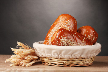 Baked bread in basket on wooden table on grey background
