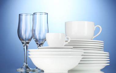Obraz na płótnie Canvas empty bowls, plates, cups and glasses on blue background
