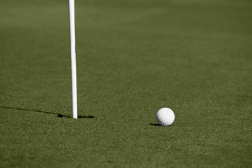 Golf ball close to hole with flagstick on putting green