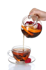 Glass teapot pouring black tea into cup isolated on white