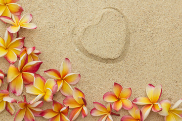 Fototapeta na wymiar Frangipani/plumeria flower frame, with print of heart, on sand