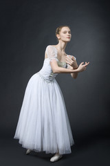 Beautiful ballerina poses in white dress, on pointes.