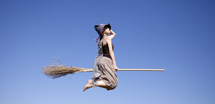 Young red-haired witch on broom flying in the sky