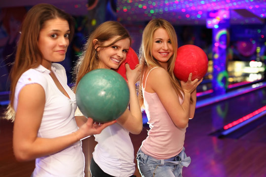 three girls with balls stand in bowling club