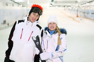 Happy husband and wife dressed in sports clothes stand with skis
