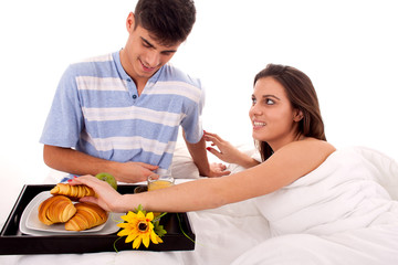 Beautiful couple having breakfast lying in the bed at home