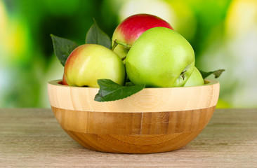 Fresh organic apples in plate on wooden table outside