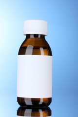 Liquid medicine in glass bottle and pills on blue background