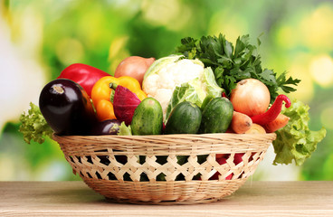Fresh vegetables in basket on  wooden table on green background