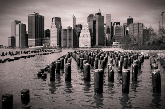 Fototapeta Skyline von Manhattan mit Holzpfählen im Wasser, schwarzweiss