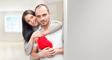 Portrait of young couple with red heart standing at their home a