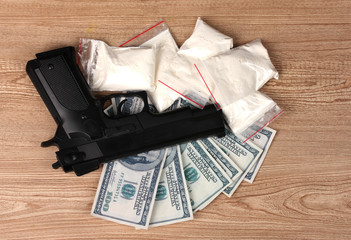 Cocaine in packages, dollars and handgun on wooden background