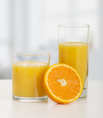 Naklejka na ściany i meble dwie szklanki soku pomarańczowego i dojrzałe pomarańcze w plasterkach