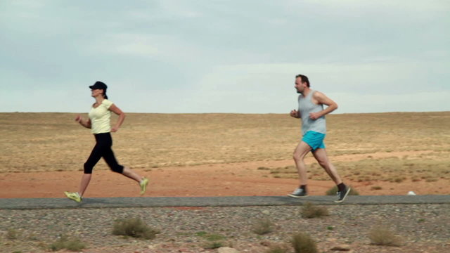 Young couple jogging on desert road, slow motion
