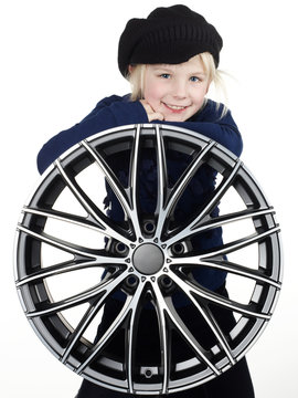 Cute blonde girl with knit cap leans over an aloy wheel