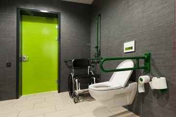 a toilet for disabled people with green bars, wheelchair