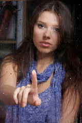 Fototapeta na wymiar young sad woman behind wet window